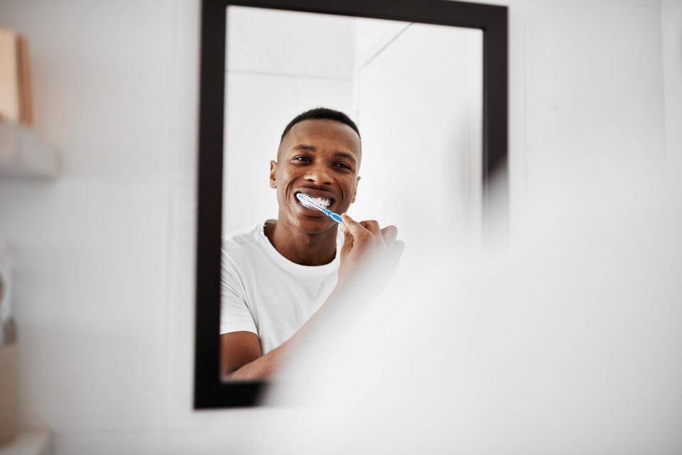 Shot of a young man brushing his teeth while looking into the bathroom mirror