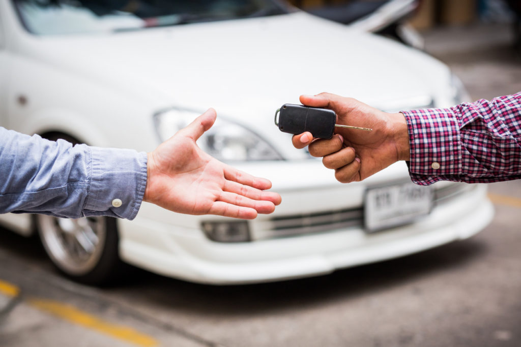 Hand giving car key on car background